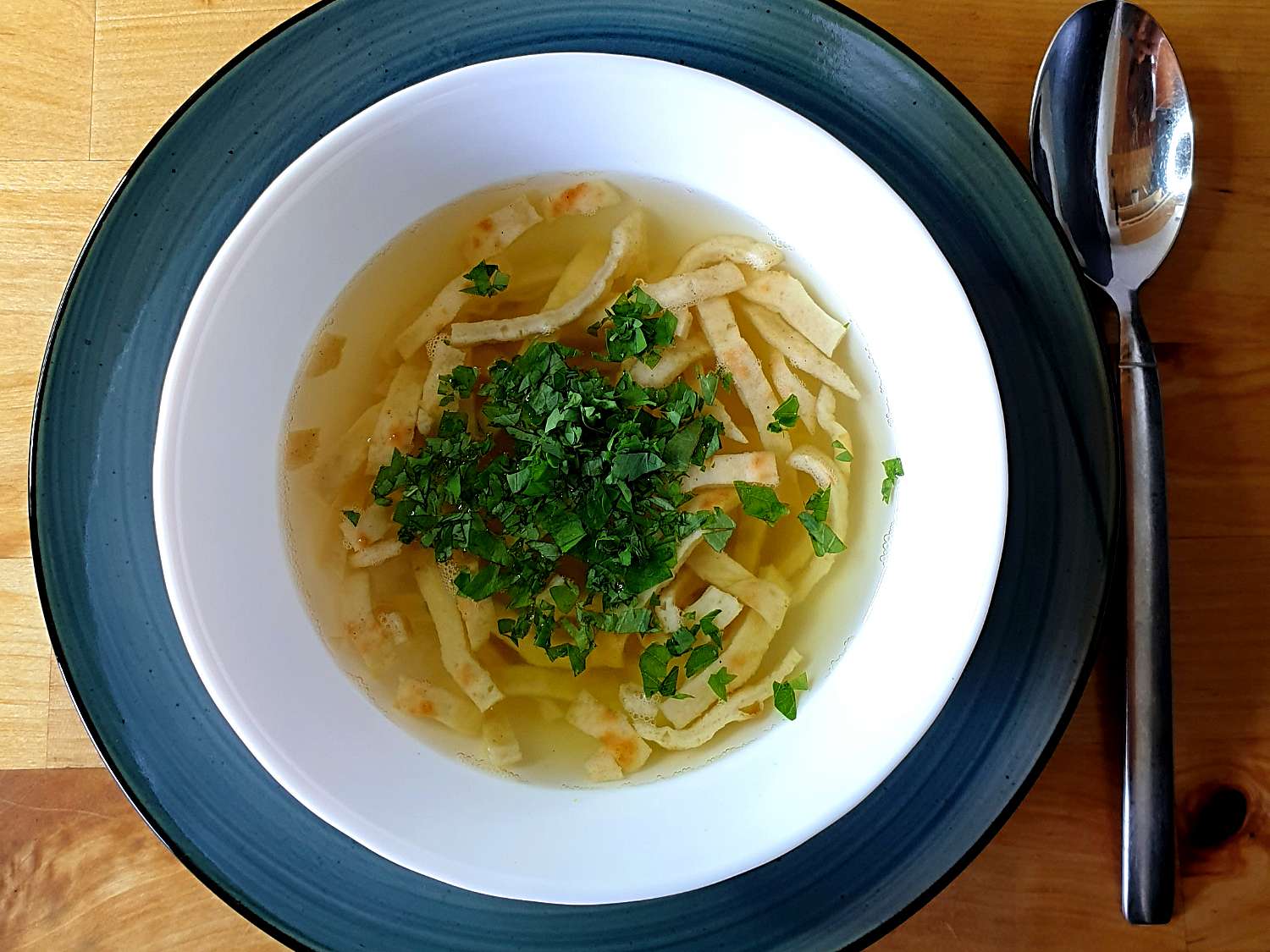 Ein Teller mit Gemüsebrühe und einer Einlage aus Pfannkuchenstreifen, garniert mit Petersilie