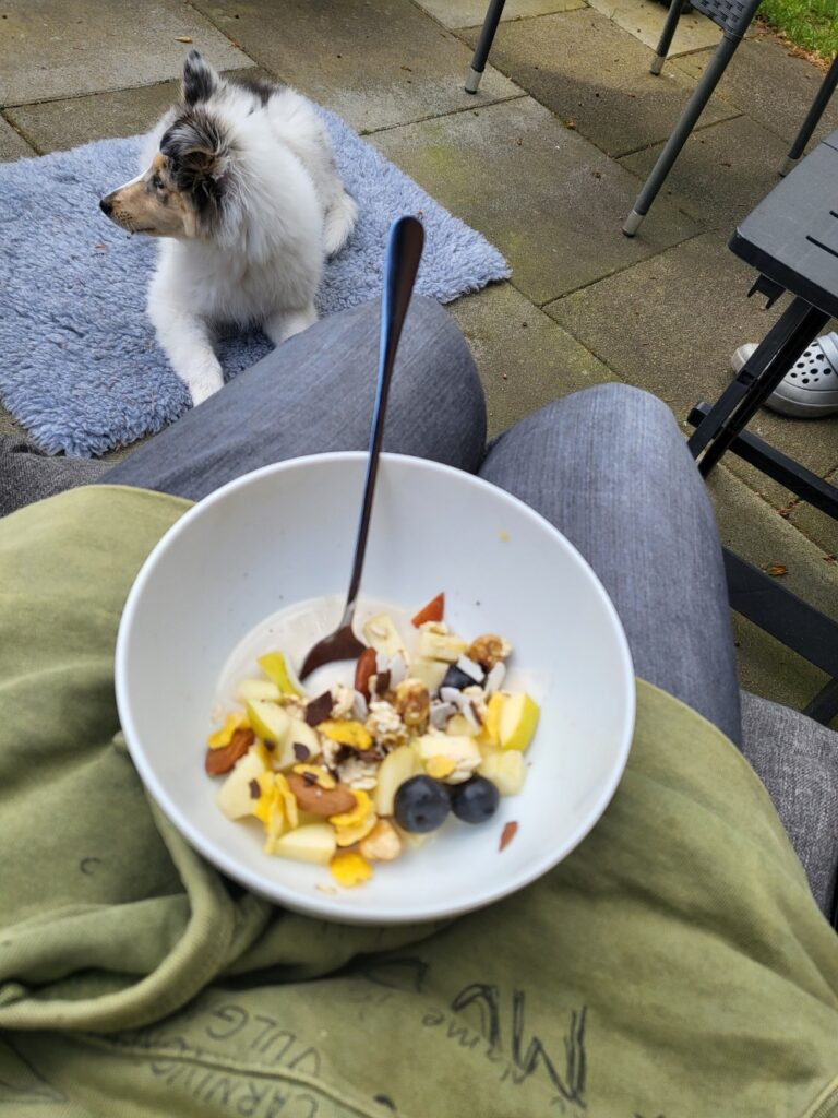 Eine Schale Müsli auf den Knien und den Welpen vor den Füßen.