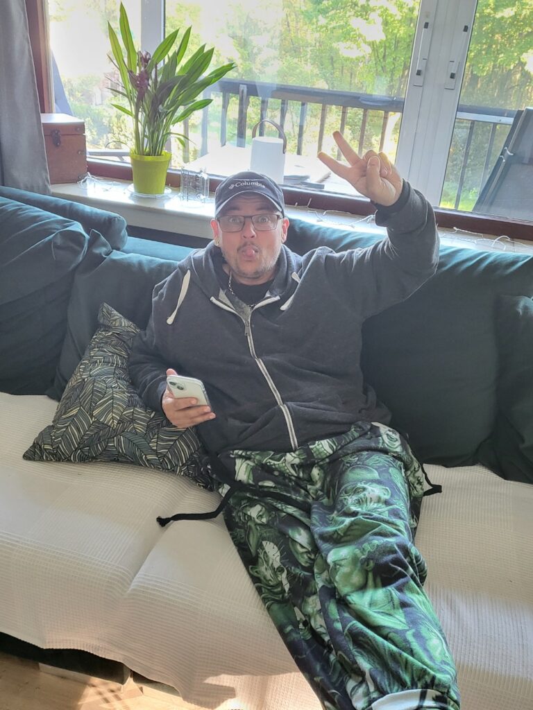 Ein Mann sitze auf einem Sofa, macht das Victory-Zeichen und steckt die Zunge raus.