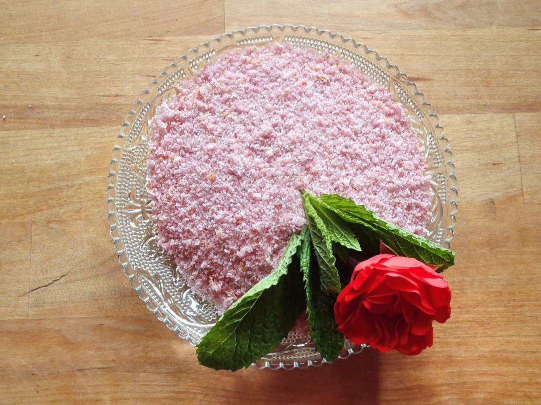 Roséfarbener Rosenzucker dekoriert mit einer Rose auf einem Glasteller